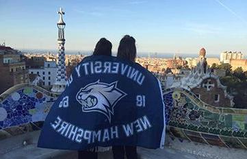 UNH students abroad with UNH flag draped across their backs